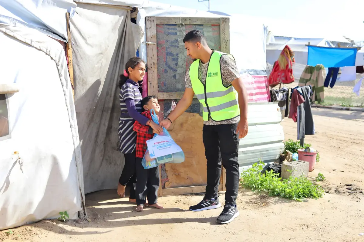 A CBB volunteer gives a food package to two children outside their shelter in a Gaza camp