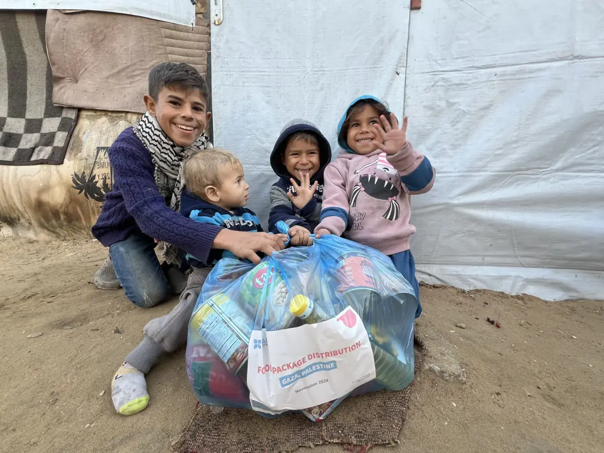 Children gathered around a CBB food package outside their tent in Gaza