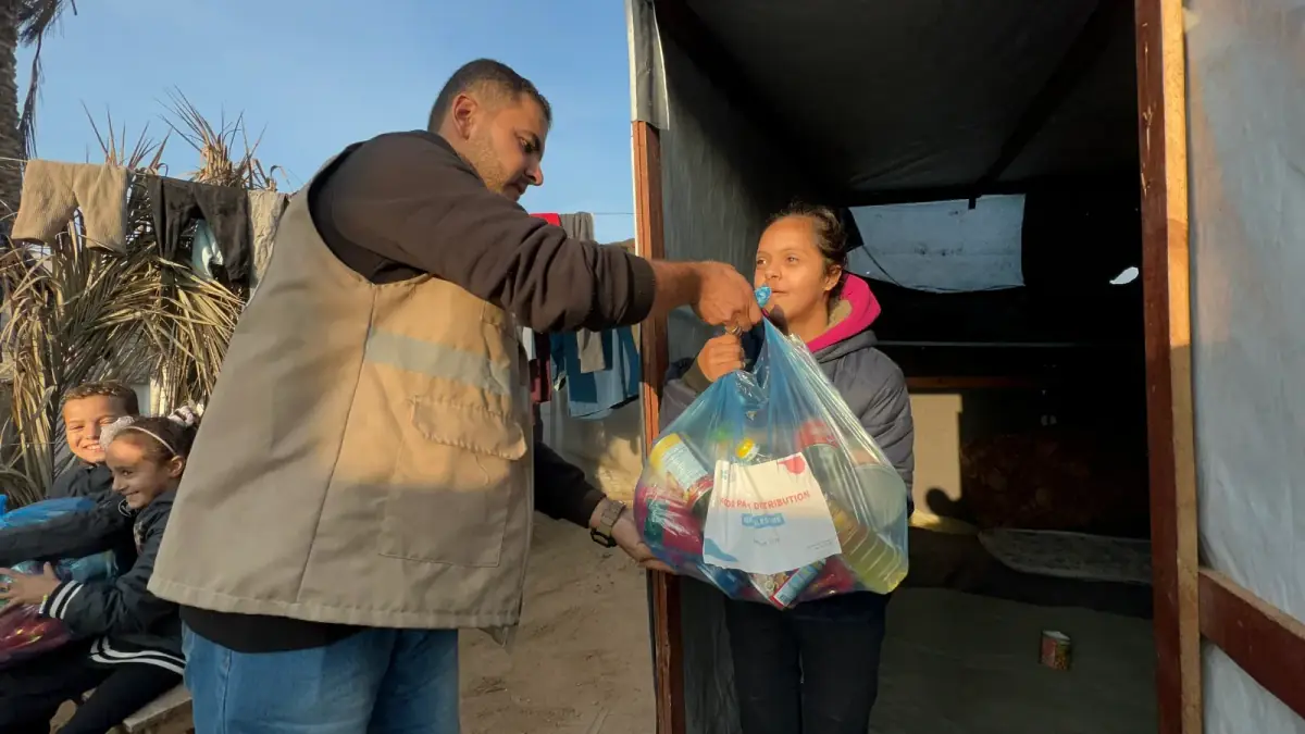 A CBB volunteer hands a food package to a girl at her shelter in a Gaza camp