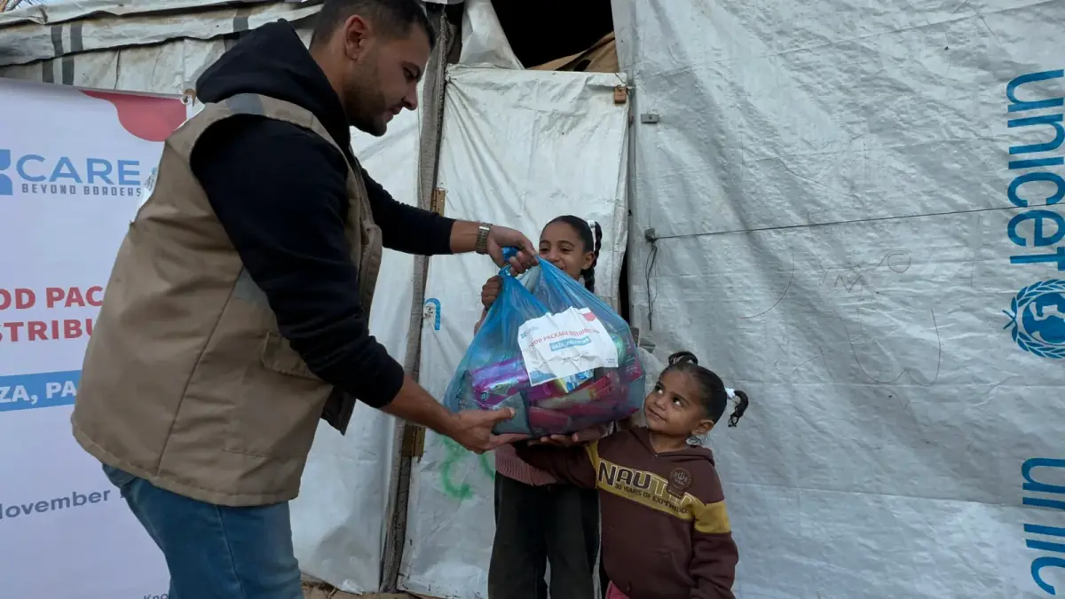 A CBB volunteer hands a food package to two young girls outside their tent in Gaza