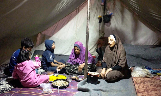 A displaced family sharing a meagre meal together inside a tent shelter at night