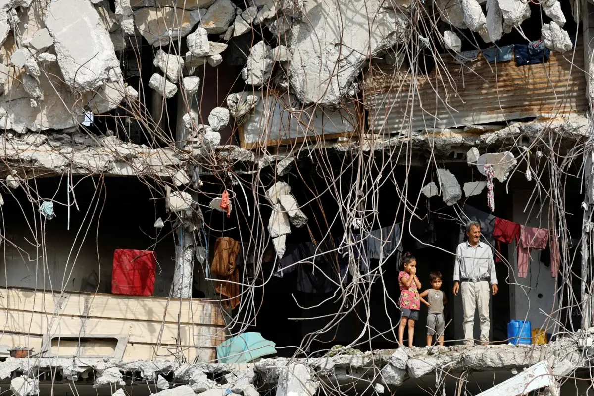 A father and his two young children stand in the wreckage of their destroyed building in Gaza