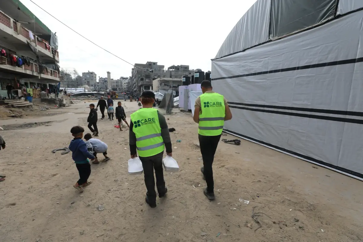 Two CBB volunteers carrying meal trays through a Gaza camp to deliver them